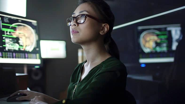 Remote work 3 great tips | medical doctor looking at scans young asian woman working at a desk with multiple monitors. She’s studying the moving data & information on the screens which consists of human body scans, MRI & CAT, and scrolling text & numbers.